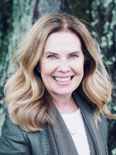 Portrait of woman facing camera and smiling with greenery behind.