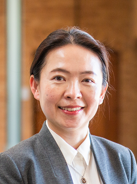 Alice Tsai smiling, standing in front of brown brick background