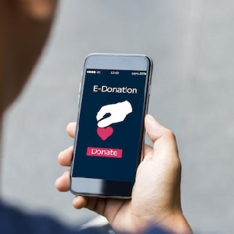 Over the shoulder shot of person holding phone with screen displaying "E-Donation"  