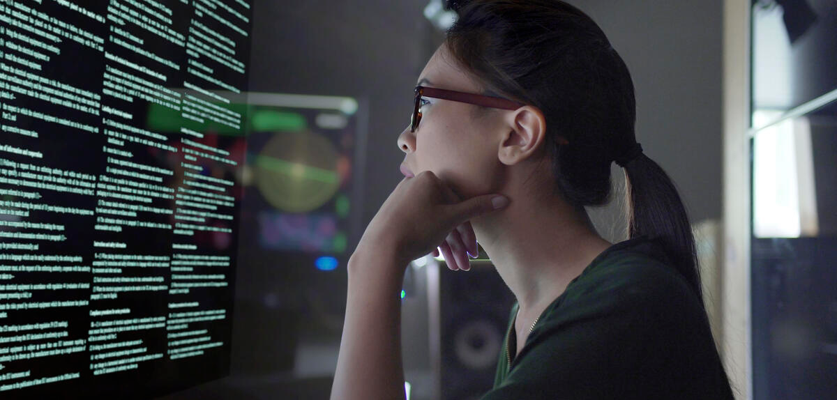 Woman with head resting on hand looking at computer monitor with lines of text on it