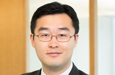 Portrait of Peng Zhao wearing black suit against an opaque window with brown beams 