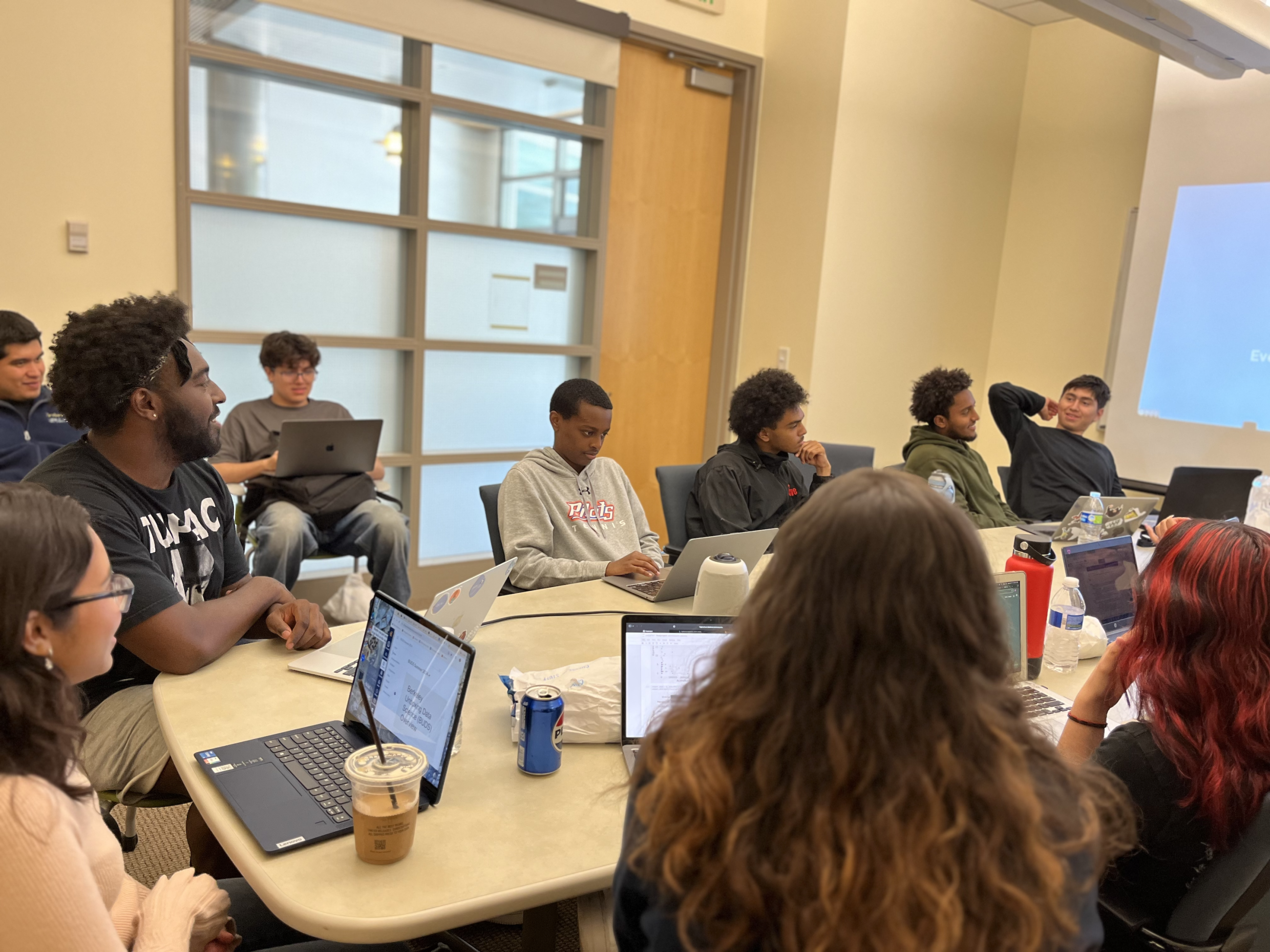 At a table, high school BUDS students sit with laptops as William Reed leads a group discussion.