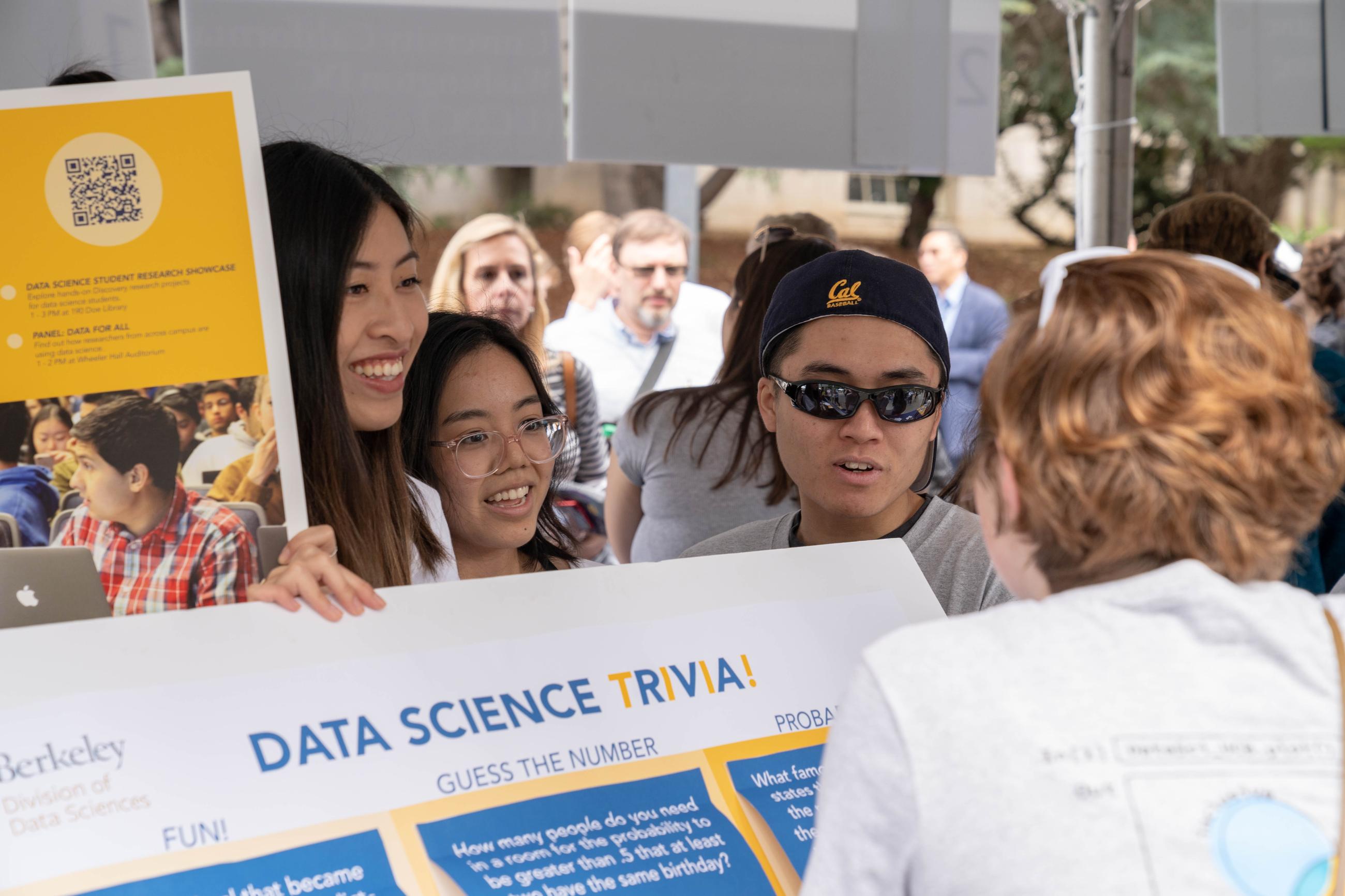 Students at Cal Day show interested person a data science trivia poster
