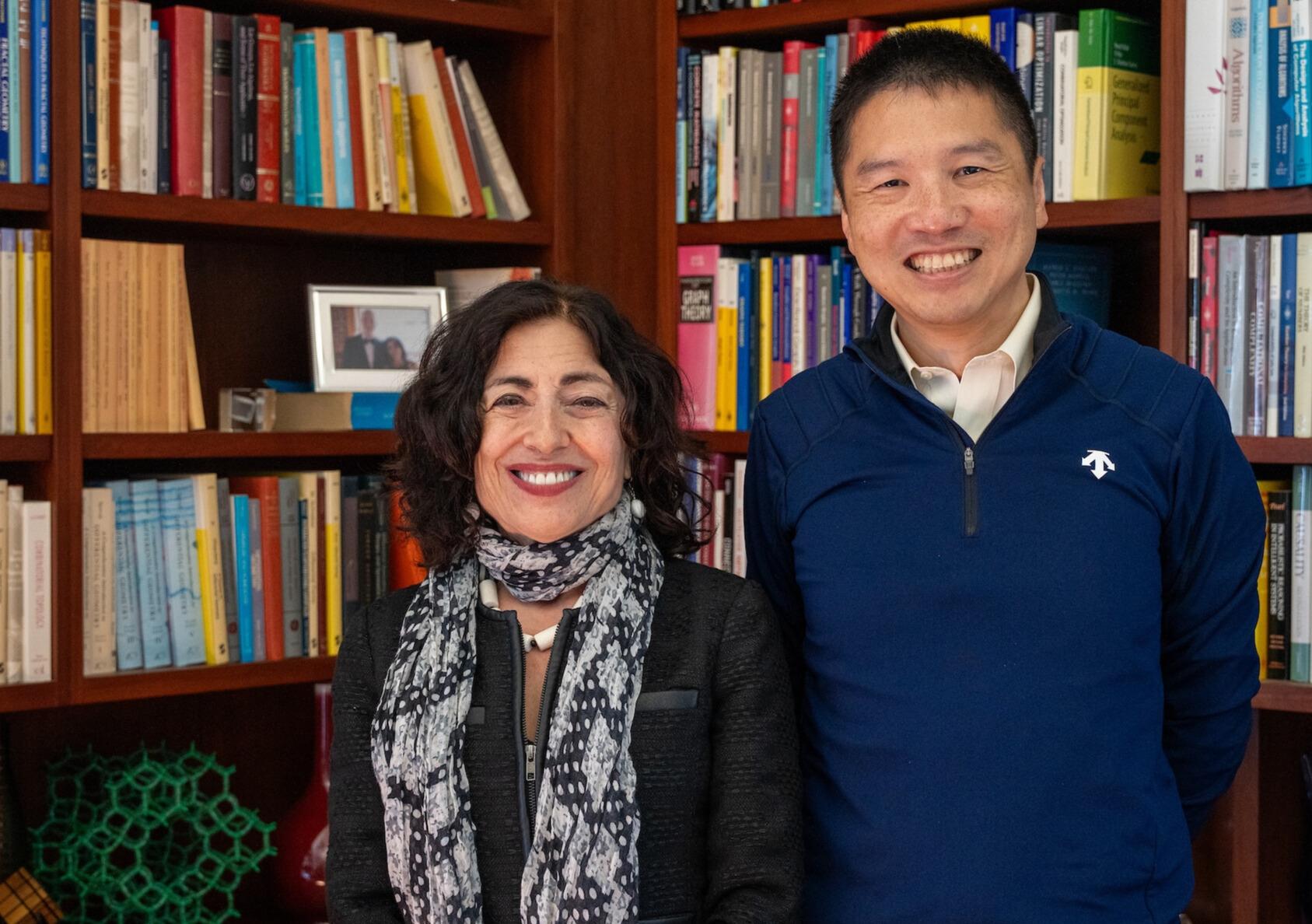 Jennifer Chayes and Hao Zhang stand in front of books in a wooden bookshelf