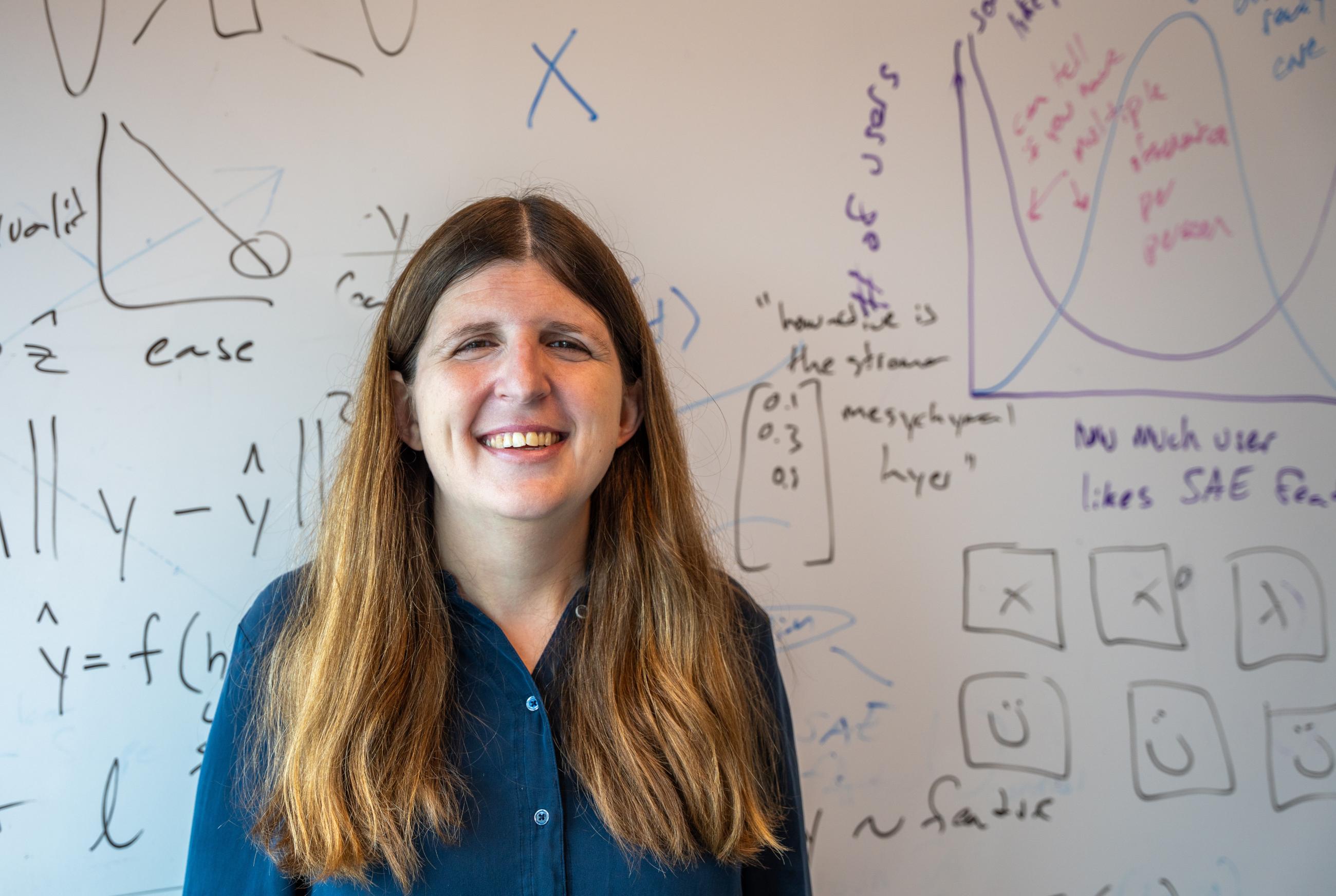Emma Pierson stands in front of a whiteboard with mathematical equations