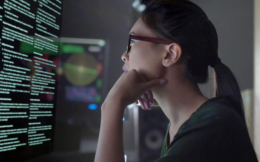 Woman with head resting on hand looking at computer monitor with lines of text on it